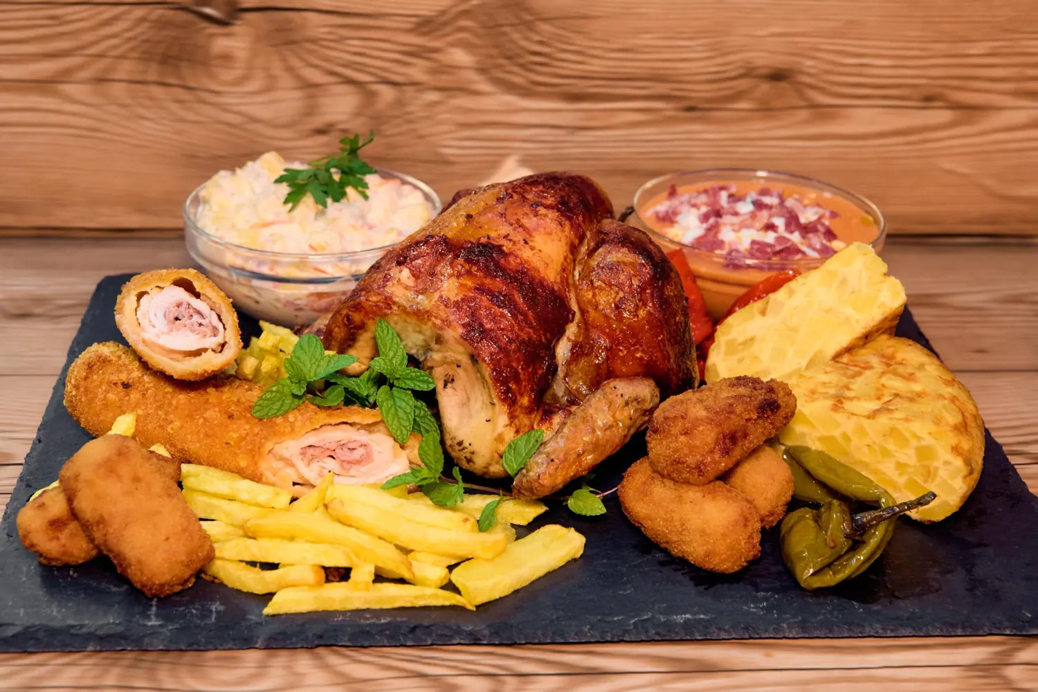 Pollo asado con croquetas, flamenquín, tortilla y ensaladillas sobre pizarra