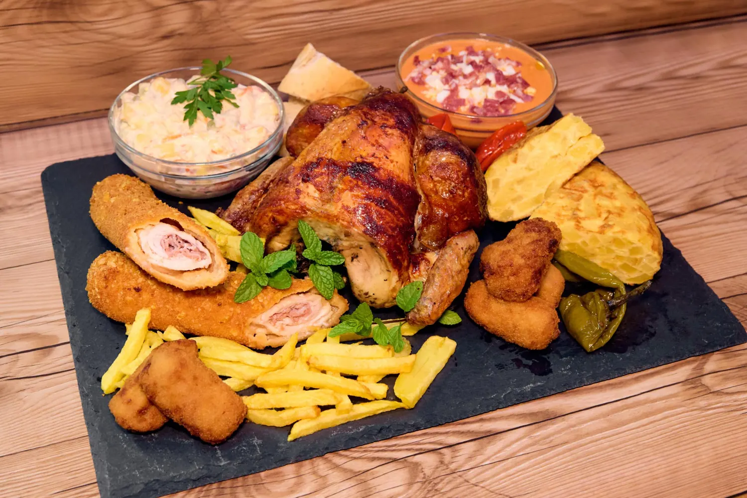 Tabla de pollo asado con guarniciones, croquetas y ensaladas